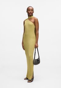 Olivovo zelené pletené maxi šaty s asymetrickým výstrihom a bočným rozparkom. V kombinácii s malou, textúrovanou čiernou kabelkou a plochými topánkami s strapcami.