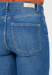 Šauras zils denim audums ar vidēju vidukļa augstumu, vienā aizmugures kabatā. Audumam ir gluda tekstūra ar smalku izbalēšanu.