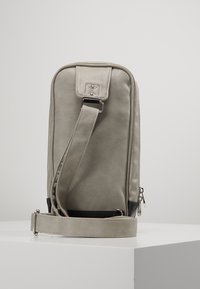 Skórzana torba na ramię w jasnoszarym kolorze, o płaskim kształcie, z regulowanym paskiem i detalem w postaci zamka, z kontrastującą czarną podstawą.