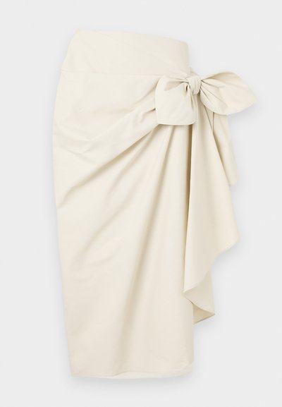 Jupe enveloppante couleur crème en tissu lisse, ornée d'un grand nœud à la taille et d'une silhouette fluide et drapée.