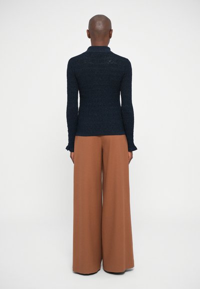 Haut à manches longues texturé bleu marine avec col, associé à un pantalon large marron, vu de dos sur fond blanc.