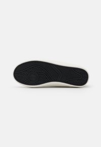 Sneaker bianco con upper in tela testurizzata, suola in gomma nera spessa con motivo di battistrada e dettagli del logo circolare.