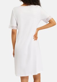 Abito bianco a maniche corte con pizzo sui bordi delle maniche; vestibilità comoda, lunghezza al ginocchio, texture liscia, scollatura tonda, design semplice.