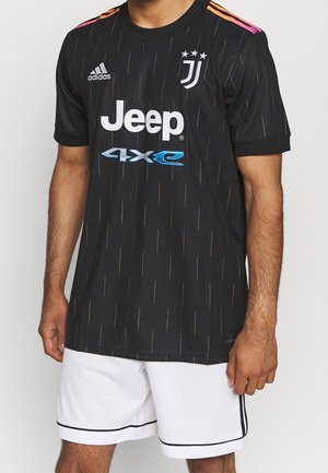Buste masculin portant un maillot de football noir de la Juventus avec les logos Jeep et Adidas, assorti à un short blanc avec un liseré noir.