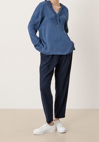 Haut bleu à capuche avec un col en V et trois boutons, associé à un pantalon bleu marine à coupe décontractée et des baskets blanches. Texture lisse dans l'ensemble.