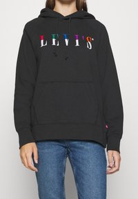 Svart hoodie med framficka, försedd med en flerfärgad "LEVI'S"-logotyp över bröstet, tillverkad av mjukt material med dragsko i huvan.