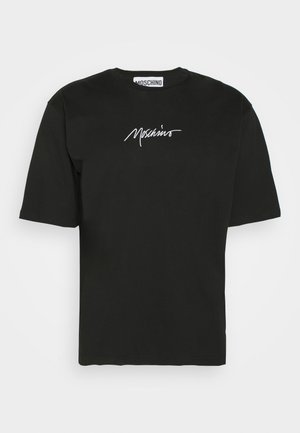 Henkilö, jolla on päällään musta t-paita, kirkkaan punaiset housut, mustat slip-on-tossut valkoisilla pohjilla ja sininen kuviollinen huivi solmittuna kaulan ympärille.