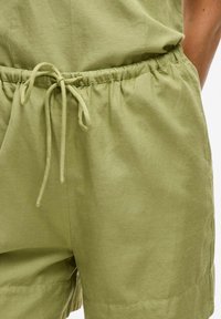 Lys grønne shorts med elastik i taljen og snøre, der har en glat tekstur og sidelommer, lavet af et åndbart stof.