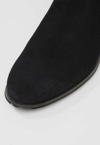 Schwarze Wildleder-Booties mit einer glatten, runden Zehenpartie und einer dünnen, eleganten Sohle. Die strukturierte Oberfläche hat ein weiches Finish ohne sichtbare Hardware.