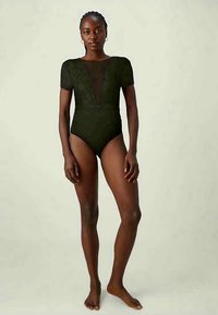 Črn bodi z kratkimi čipkastimi rokavi in globokim dekoltejem, ki ima zapleteno čipkastovo obrobo okoli območja prsi. Gladek, prilegan dizajn.