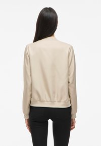 Beige bomberjakke med en glatt satinfinish, ribbede mansjetter og bunn, og et enkelt design. Ingen synlige dekorasjoner eller mønstre.
