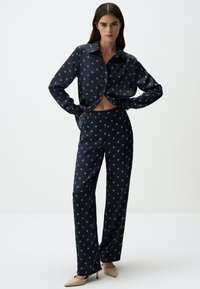 Marineblauw zijde pyjama set met sterrenprint; langetermijn knoopsluiting shirt en bijpassende brede broek. Gladde textuur en relaxte pasvorm.