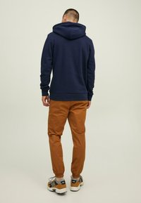 Felpa navy con cappuccio regolabile, abbinata a pantaloni tapered di un marrone chiaro e sneakers multicolor. Tessuto morbido con una vestibilità comoda.