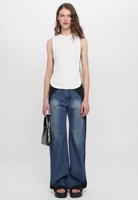 White sleeveless top with a round neckline, paired with wide-leg blue jeans featuring black side panels, and black glossy handbag.