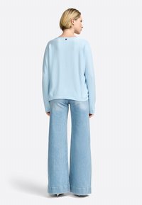 Himmelblaues Sweatshirt aus einem weichen Stoff mit lockerer Passform, kombiniert mit weit geschnittenen hellen Denim-Jeans, die einen rohen Saum und eine leichte Ausbleichung aufweisen.