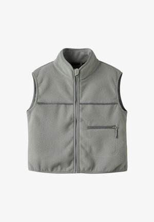 Pilkas vilnos liemenė su aukštu apykakle, pilnu priekiniu užtrauktuku, dviem horizontaliais krūtinės siūlėmis ir užtrauktuku užsegama kišene kairėje pusėje.