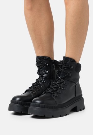 Bottines en cuir noir avec un col en chaussette texturé noir, un laçage sur le devant et une semelle épaisse segmentée. Équipées d'une fermeture éclair latérale pour un enfilage facile.