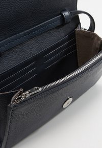 Tmavě modrá kožená kabelka se zipovou kapsou, vnitřními sloty na karty a texturovaným povrchem; má kovové zacvakávání.