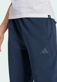 Navyblauwe sportbroek van zachte stof, met een discrete zijzak en een grijs Adidas-logo op de linkerdij.