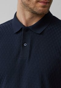 Marineblauwe polo shirt met een textuurpatroon, een klassieke kraag en twee knopen bij de hals. Ontworpen met een getailleerde pasvorm.