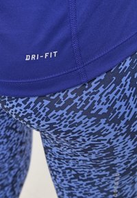 Modrý sportovní top s nápisem „DRI-FIT“, doplněný vzorovanými legínami v odstínech modré s geometrickým motivem a strukturovanou látkou.