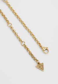 Collana in metallo dorato con maglie tonde, chiusura a gancio e pendente triangolare con il logo "GUESS".