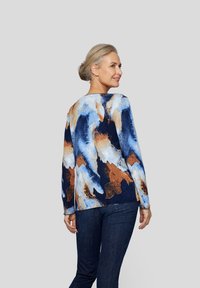 Blaues und orangenes, abstraktes, gemustertes Langarmhemd mit rundem Halsausschnitt, von hinten gezeigt, kombiniert mit dunkelblauben Jeans.