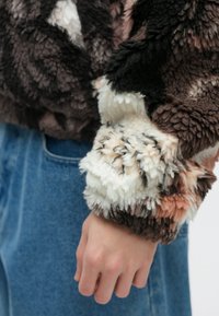 Maglione corto morbido e multicolore con tonalità di nero, marrone, bianco e pesca. Presenta un tessuto testurizzato e morbido con polsini larghi.