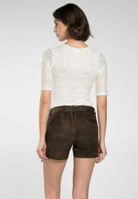Weißes Oberteil mit Spitzenmuster und kurzen Ärmeln, kombiniert mit braunen Wildleder-Shorts mit Zugband und dezenten gelben Pipings.