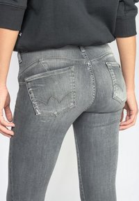 Osoba v bledě šedých džínách a černém tričku s dlouhým rukávem, ukazující zadní kapsu a oblast pasu.