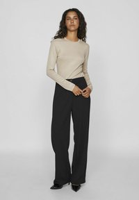 Beige langermet topp kombinert med høyt liv svarte bukser. Toppen er tettsittende, og buksene har en vid benkant med knappeåpning.
