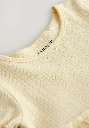 Lichtgeel katoenen top met een geribbelde textuur, voorzien van een ronde halslijn en een delicate kanten rand langs de zoom. Merknaam zichtbaar aan de binnenkant.