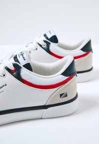 Białe skórzane sneakersy z granatowymi i czerwonymi akcentami. Cechy to zamszowa zakładka na pięcie, teksturowana gumowa podeszwa oraz sznurowany design.