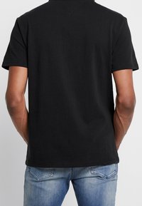 Černé bavlněné tričko s krátkými rukávy, kulatým výstřihem a hladkým zadním dílem. Materiál je měkký s hladkou strukturou.