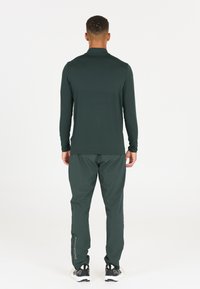 Langarmige donkergroene sporttop, gecombineerd met bijpassende taps toelopende broek, met een gladde textuur en reflecterende accenten op de pijp.