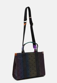 Färgglad tote-väska med svart tyg som har ett vågigt mönster. Svarta handtag och ett avtagbart band med färgglada detaljer.