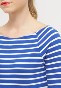 Haut rayé bleu et blanc avec une encolure bateau, en tissu doux, présente une coupe ajustée et des coutures d'épaule discrètes.