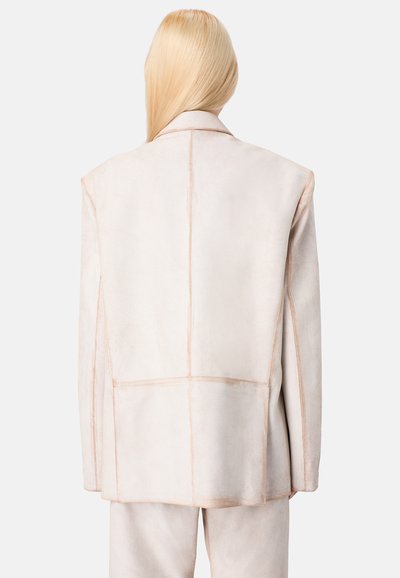 Beiger Wildleder-Blazer mit ausgeprägten Schulterpartien, sichtbaren Nähten und klaren Linien. Verfügt über eine glatte Textur und eine taillierte Passform.