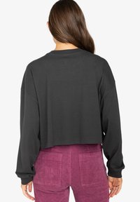 Cropped black long-sleeve sweatshirt with a round neckline and dropped shoulders, paired with pink corduroy pants featuring back pockets.