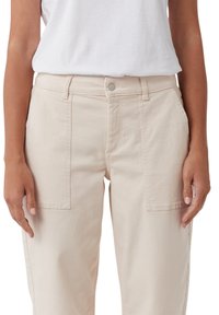Beżowe bawełniane spodnie cargo o luźnym kroju, z dużymi kieszeniami z przodu i klasycznym zapięciem na guzik. Gładka faktura z widocznym stębnowaniem.