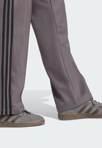 Grå treningsbukser med svarte vertikale striper, kombinert med grå joggesko med brune striper og teksturerte såler.