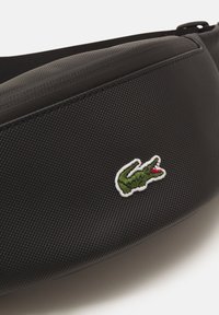 Crna torba teksture izrađena od izdržljivog materijala sadrži zeleni krokodil u okviru bijele boje. Elegantan dizajn s zatvaračem.