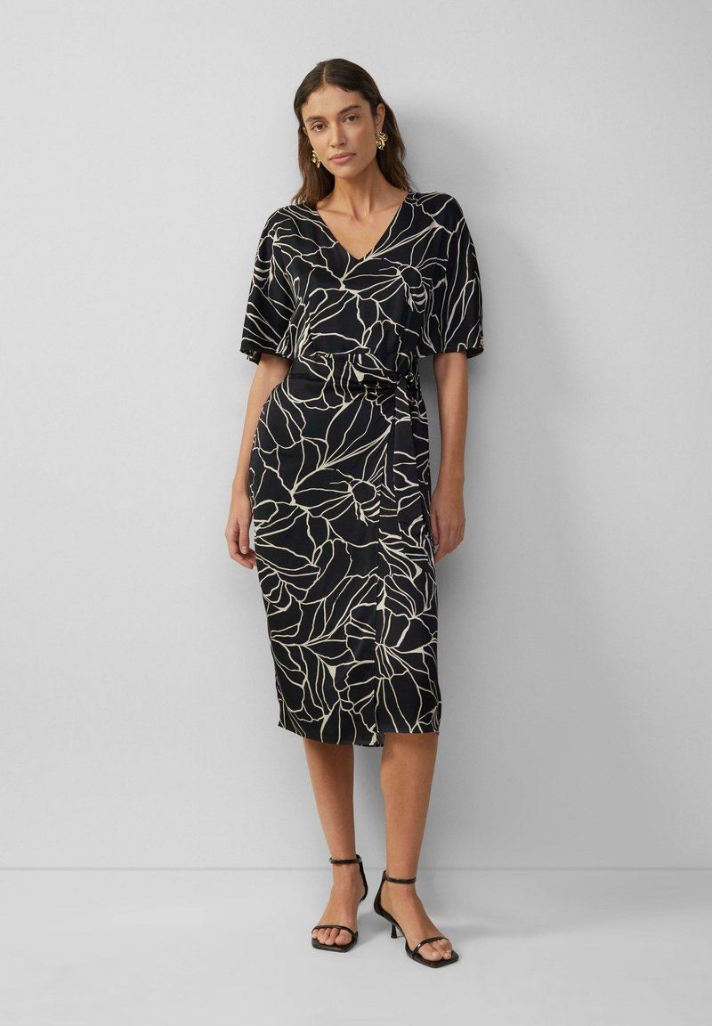 Robe noire avec un décolleté en V et des manches courtes, ornée d'un motif botanique blanc. Le tissu a une texture lisse et une taille ceinturée.
