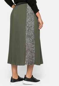 Jupe plissée vert olive avec un panneau à imprimé léopard noir et blanc. Dotée d'une taille ajustée et associée à des baskets noires.