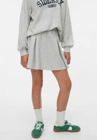Sweat-shirt gris avec l'inscription "SIDERICK", associé à une jupe plissée grise assortie. Des baskets vertes et des chaussettes blanches à bord festonné complètent le look.