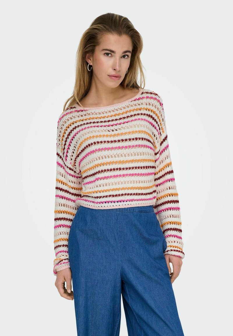 Gestreepte haak gebreide trui in crème, oranje, roze en bordeauxrood met een wijd decolleté en lange mouwen, gecombineerd met blauwe spijkerbroek.