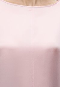 Gros plan d'une personne portant un haut en tissu satiné rose clair avec une encolure ronde et une couture verticale visible au centre.