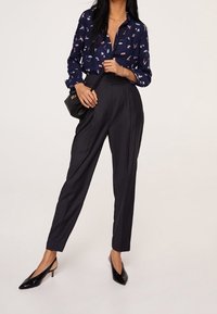 Camicia blu navy con design a motivi, pantaloni neri a vita alta e tacchi neri. Il look è completato da una piccola borsa a tracolla nera.