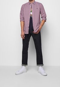 Červená a bílá kostkovaná košile s límečkem na knoflíky, nošená přes námořnicky modré tričko s grafikou, doplněná tmavými džínami a bílými teniskami.