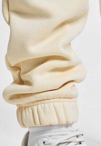 Pantaloni de trening galbeni deschis, dintr-un material moale și texturat, cu un elastic ribbat în talie și la glezne, asortați cu adidași albi.